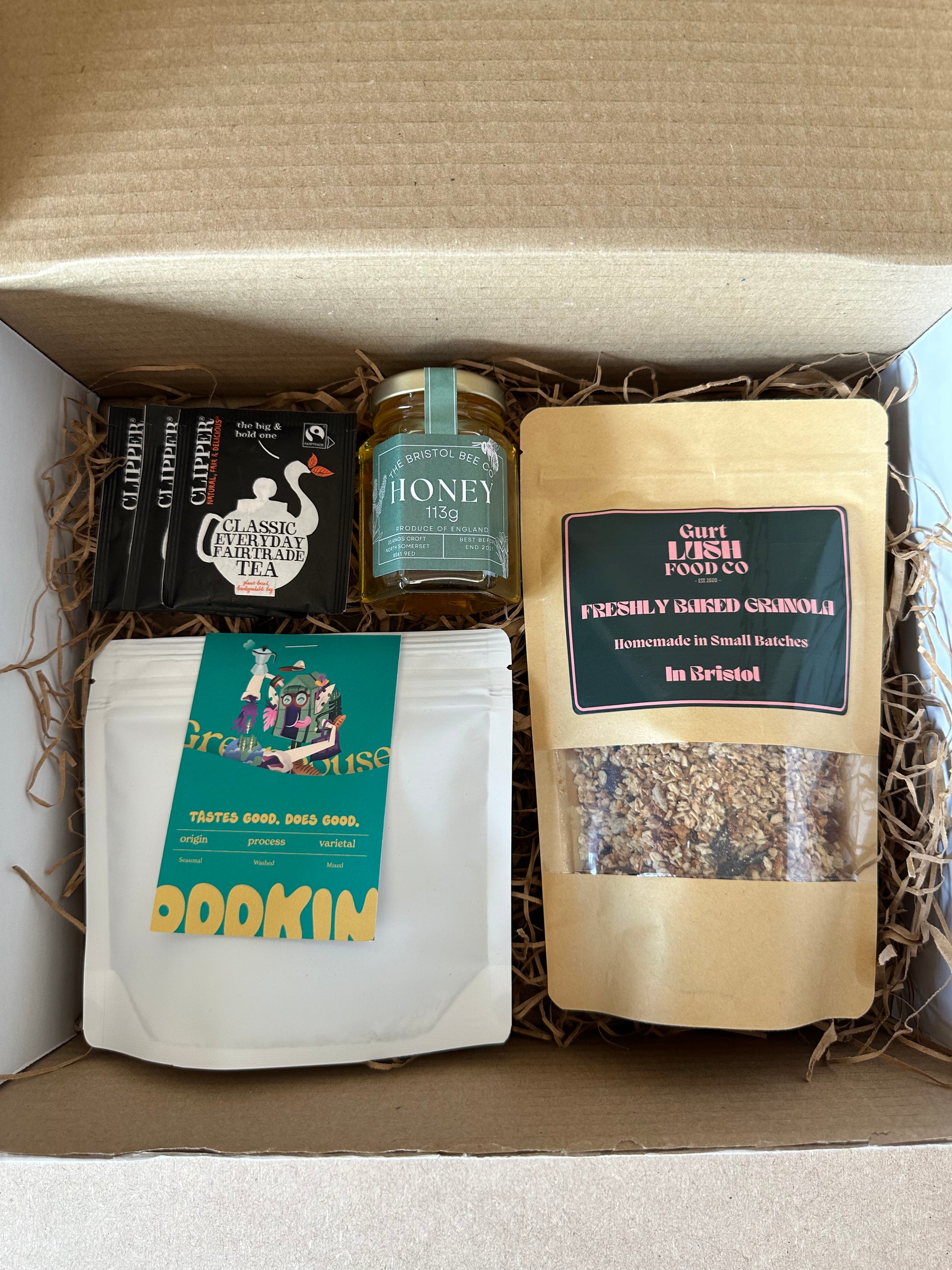 An open gift box displaying a variety of food items including honey, granola, coffee, and tea, with packaging that indicates they are locally sourced from Bristol.