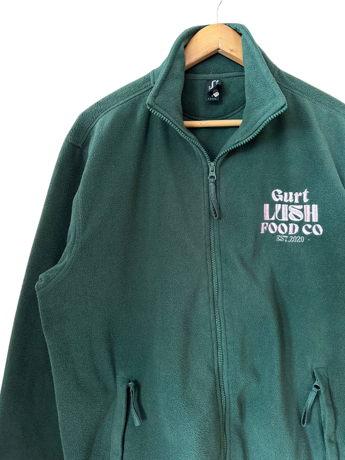 Green fleece vest with 'Gurt Wish Food Co' logo on a hanger against a white background
