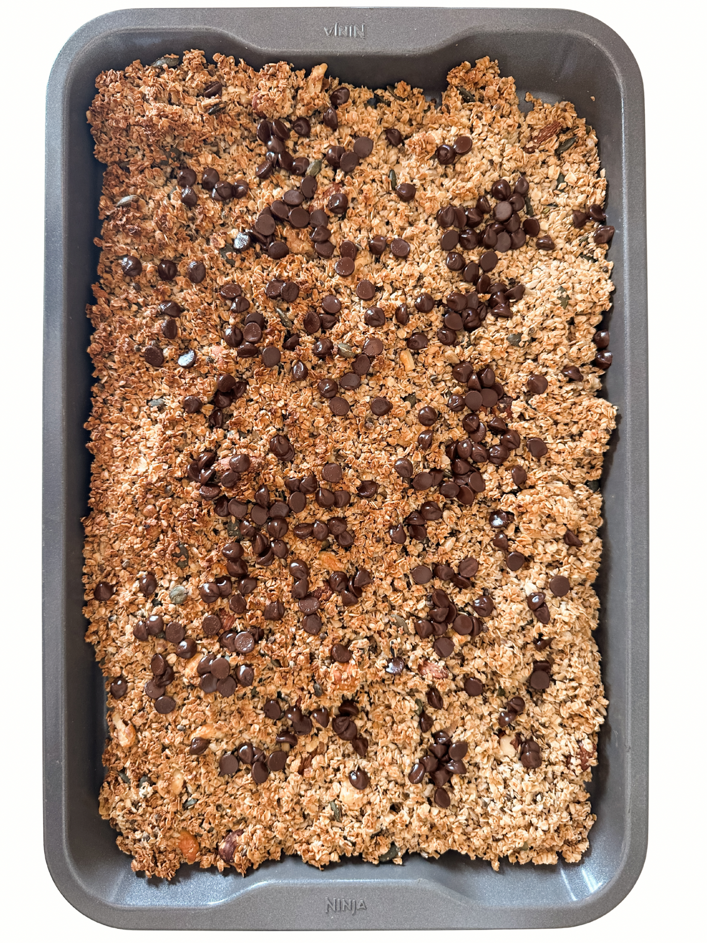 Baked oatmeal or granola bar mixture with chocolate chips in a baking tray.