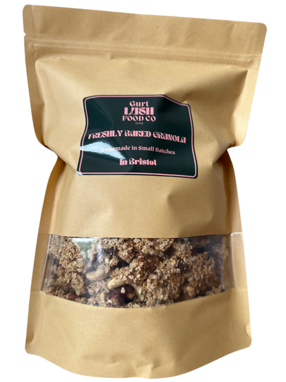 A paper bag of freshly baked granola by Gurt Lush Food Co with a clear window showing the granola inside, labeled as 'The OG' with nuts, seeds, and sultanas.
