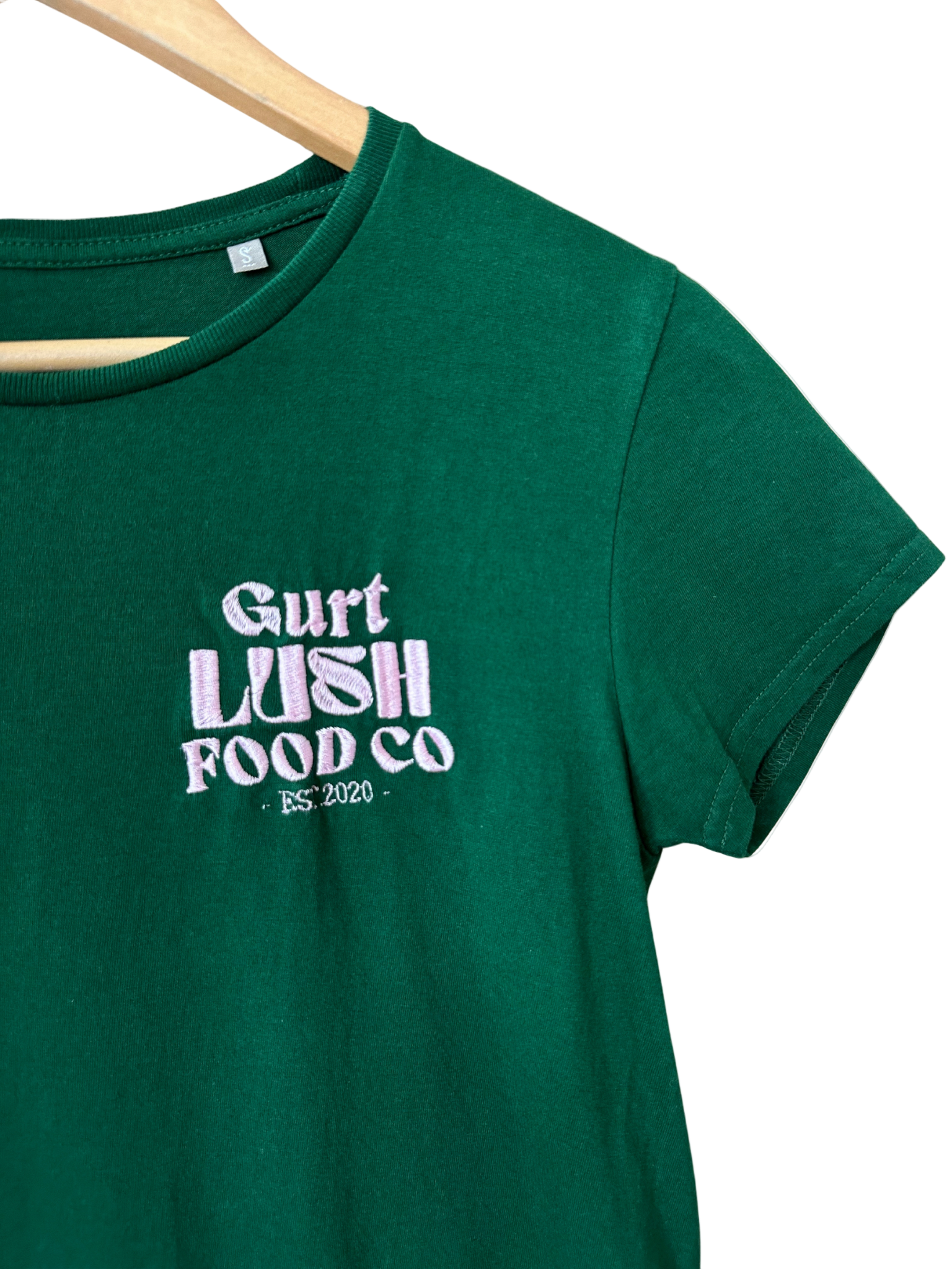 Green t-shirt with 'Gurt Lush Food Co' text on a wooden hanger