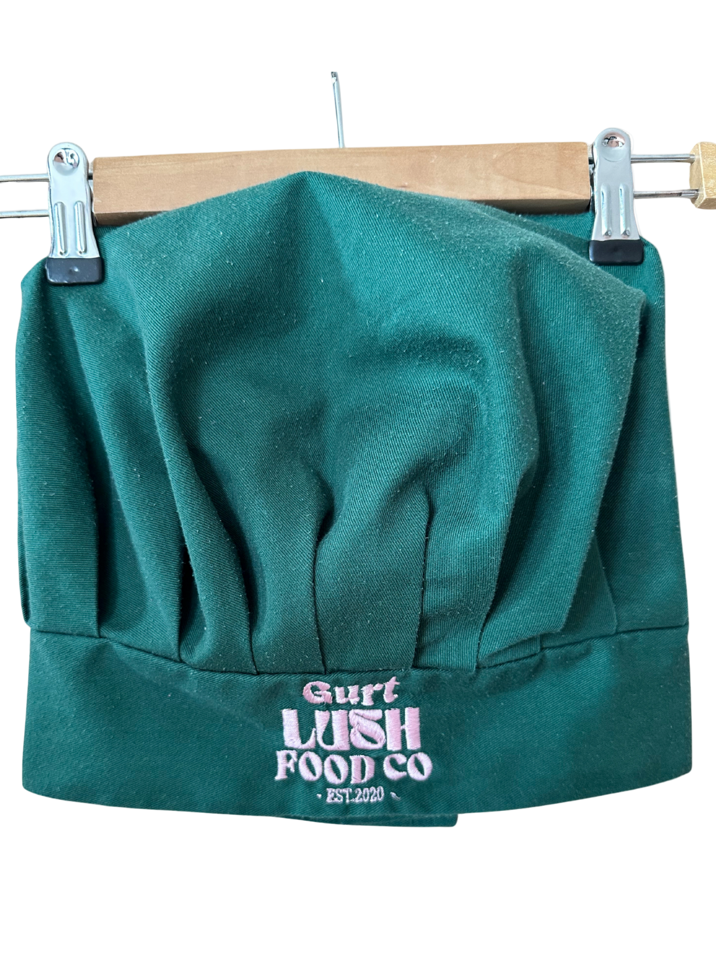 Green chef's hat with 'Gurt Lush Food Co' logo on a wooden hanger.