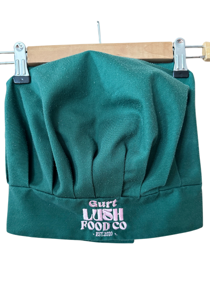 Green chef's hat with 'Gurt Lush Food Co' logo on a wooden hanger.