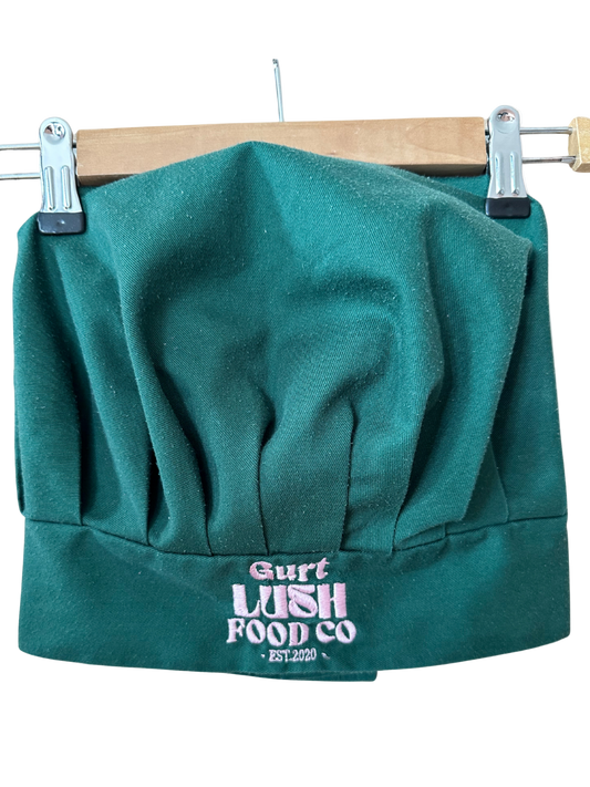 Green chef's hat with 'Gurt Lush Food Co' logo on a wooden hanger.